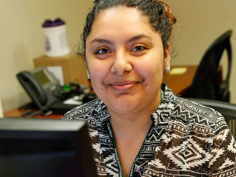 Maribel smiles at the camera from behind her desk.