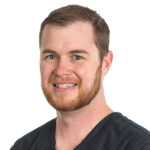 Wyatt flashes a big smile for his headshot photo, in scrubs.