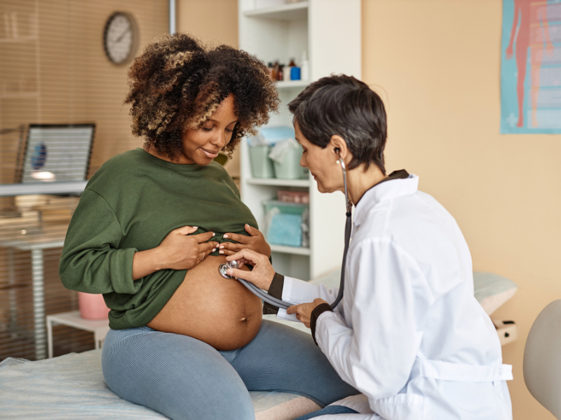 a pregnant woman at a checkup where a doctor is checking her baby's heartbeat with a stethoscope