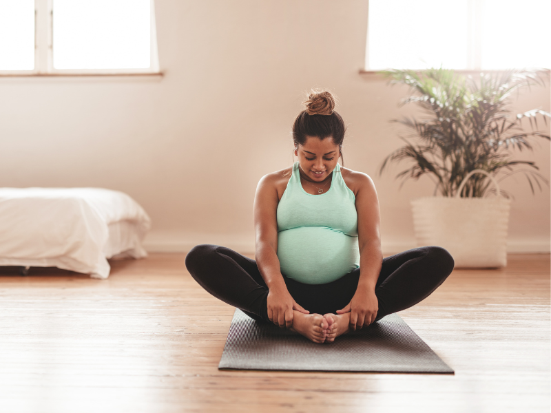 a pregnant woman sitting on the ground cross-legged, stretching her hips