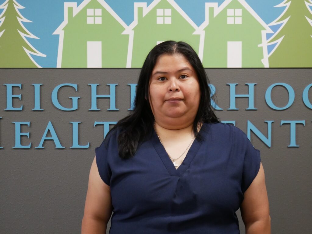 A Latina woman poses for the camera in front of an NHC sign