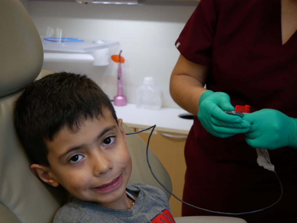 a child smiling while sitting in a dental exam chair
