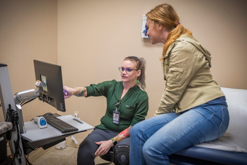 a medical assistant explaining a care plan on a computer with a patient sitting on the exam table
