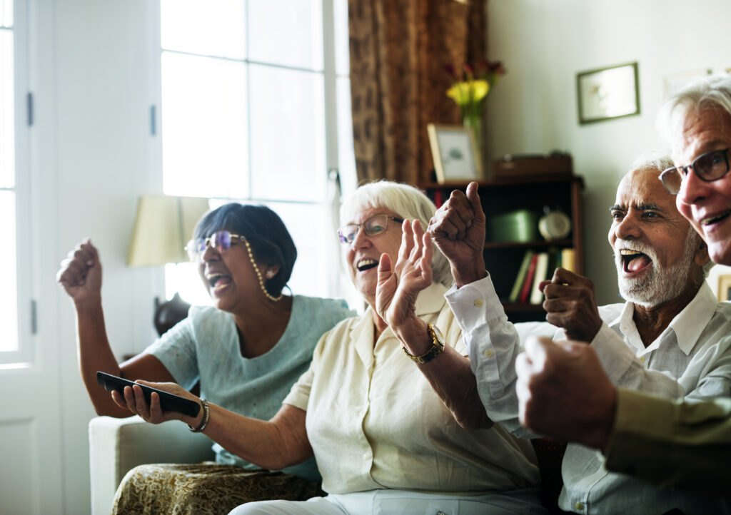 Senior people watching televison together four seniors laughing and cheering