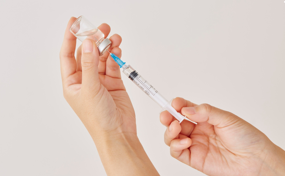 hands holding a needle, syringing out the liquid in the container