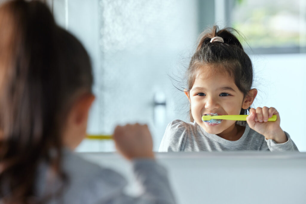 girl-child-mirror-brushing-teeth-bathroom-hygiene-with-wellness-growth-gingivitis-prevention-home-young-kid-reflection-tooth-cleaning-with-development-foam-healthy-gums Child brushing teeth at home as part of daily oral health routine.