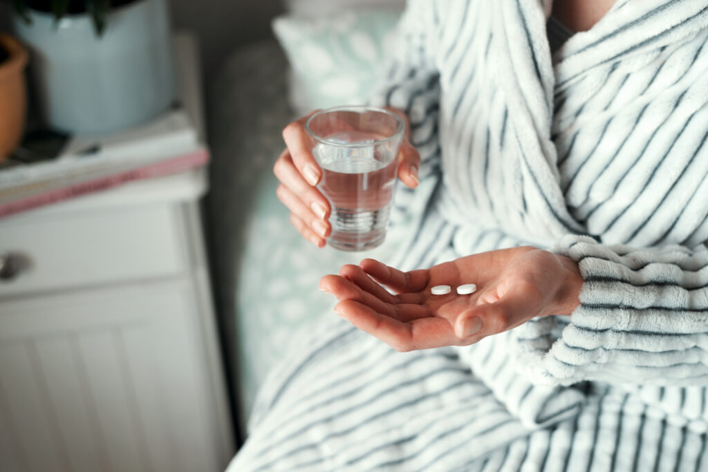 a person wearing a robe and sitting with a glass a water with medication in their other hand
