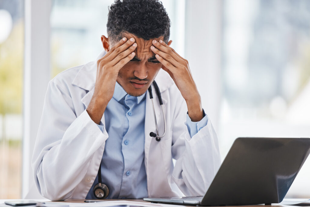 frustrated doctor putting his head in his hands while sitting in front of a laptop
