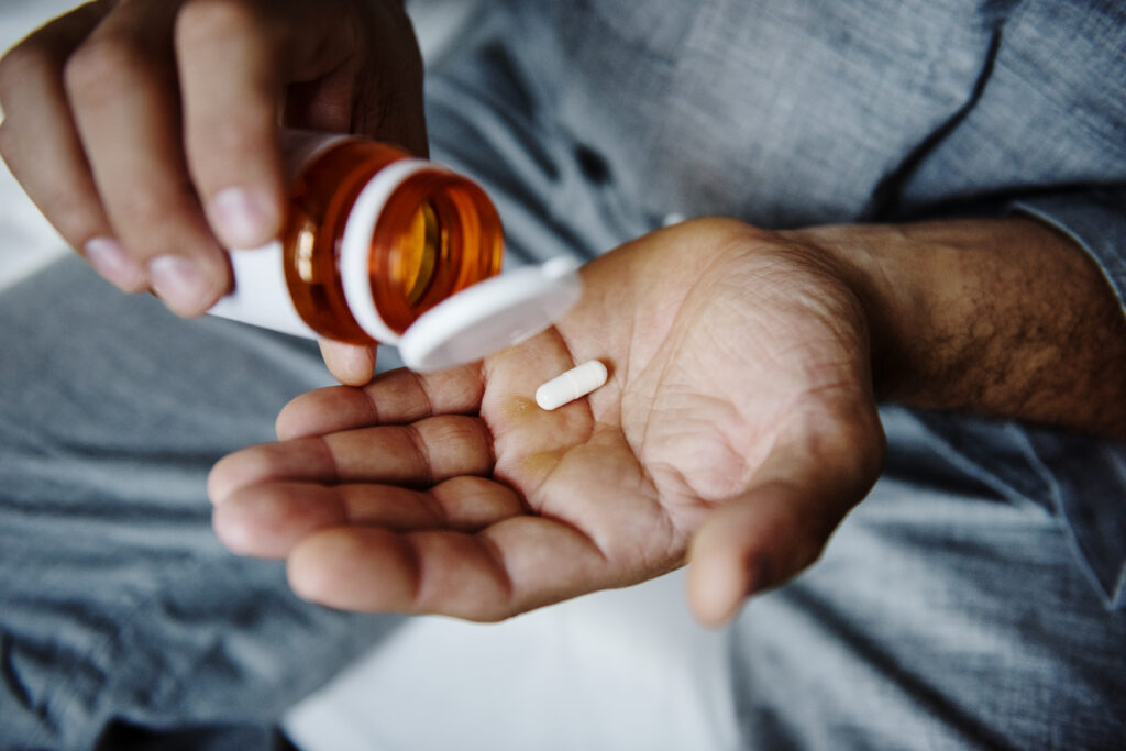 a person pouring one pill into their hand from a prescription bottle
