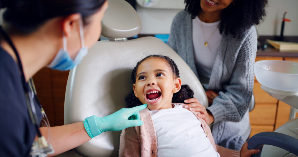a dentist pointing at a child's mouth who is sitting in the exam chair