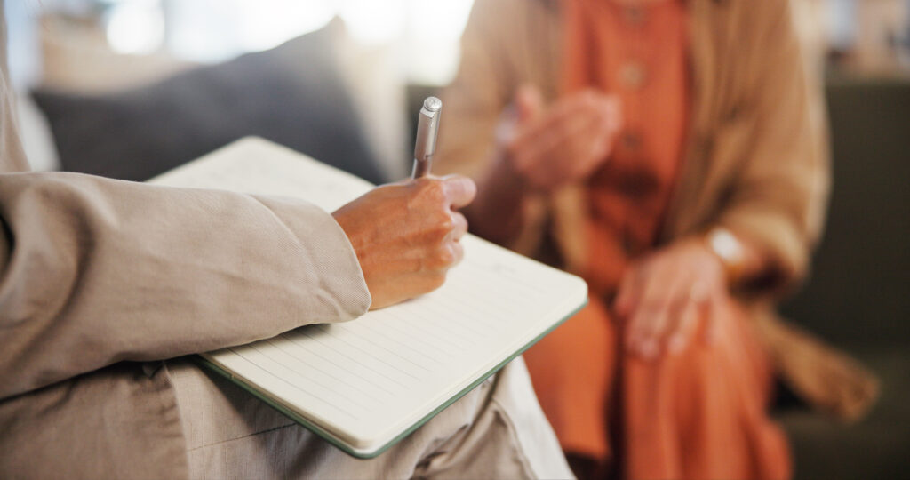 a behavioral health consultant taking notes in a notebook while talking with a patient