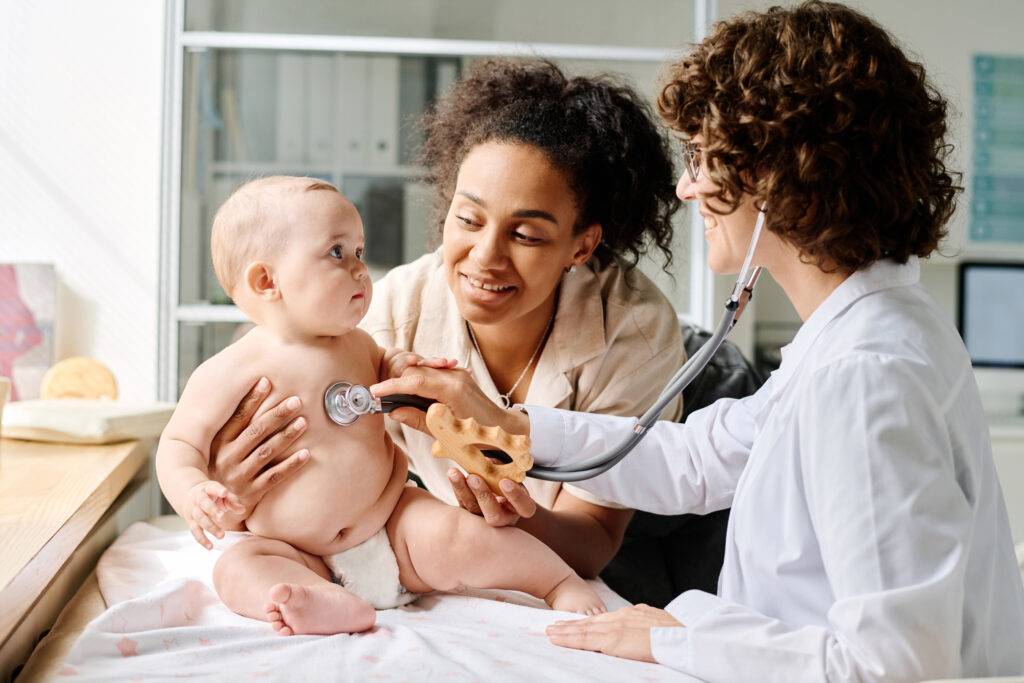 Pediatrician listens to a baby's heartbeat with a stethoscope while the mom holds the baby upright during a medical exam