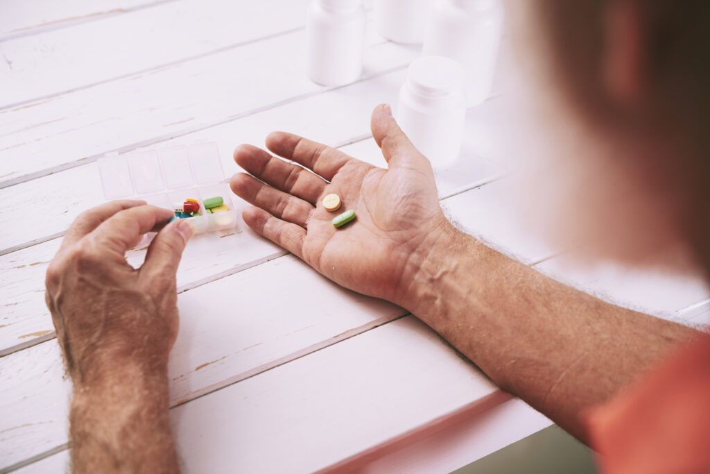 An elderly man is following his medication adherence plan by taking the medication he needs to take on this day