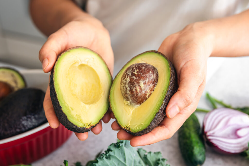 person holding two halves of an avocado