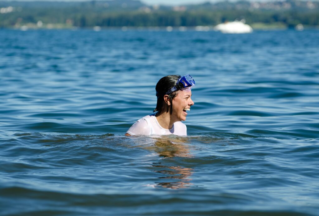 a person swimming in a lake with goggles on, smiling