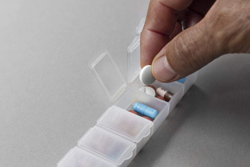 a hand putting medication into a pill organizer
