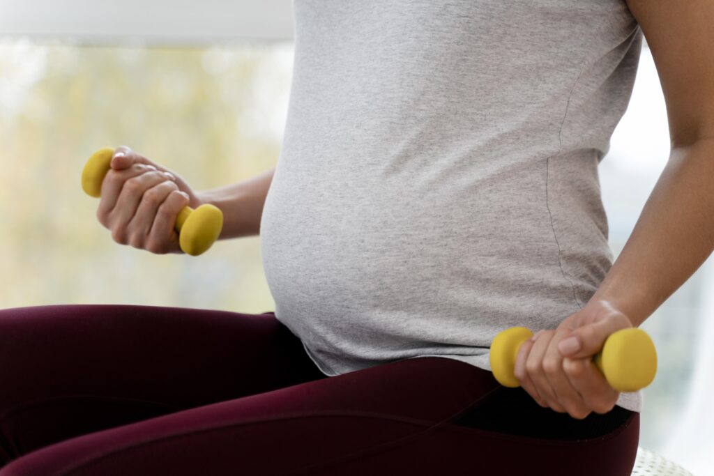 a close-up on a pregnant person's stomach while they're holding weights in their hands
