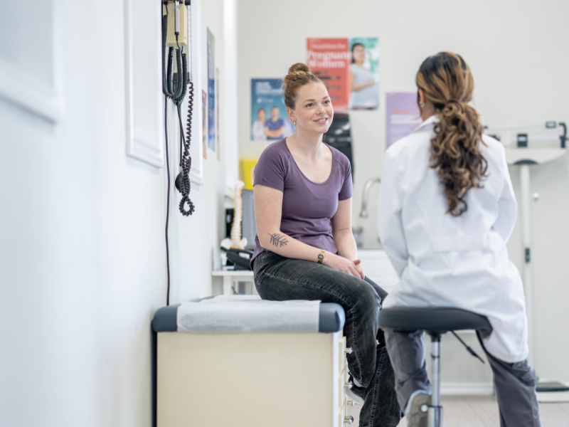 a patient sitting on an exam table while talking to their doctor