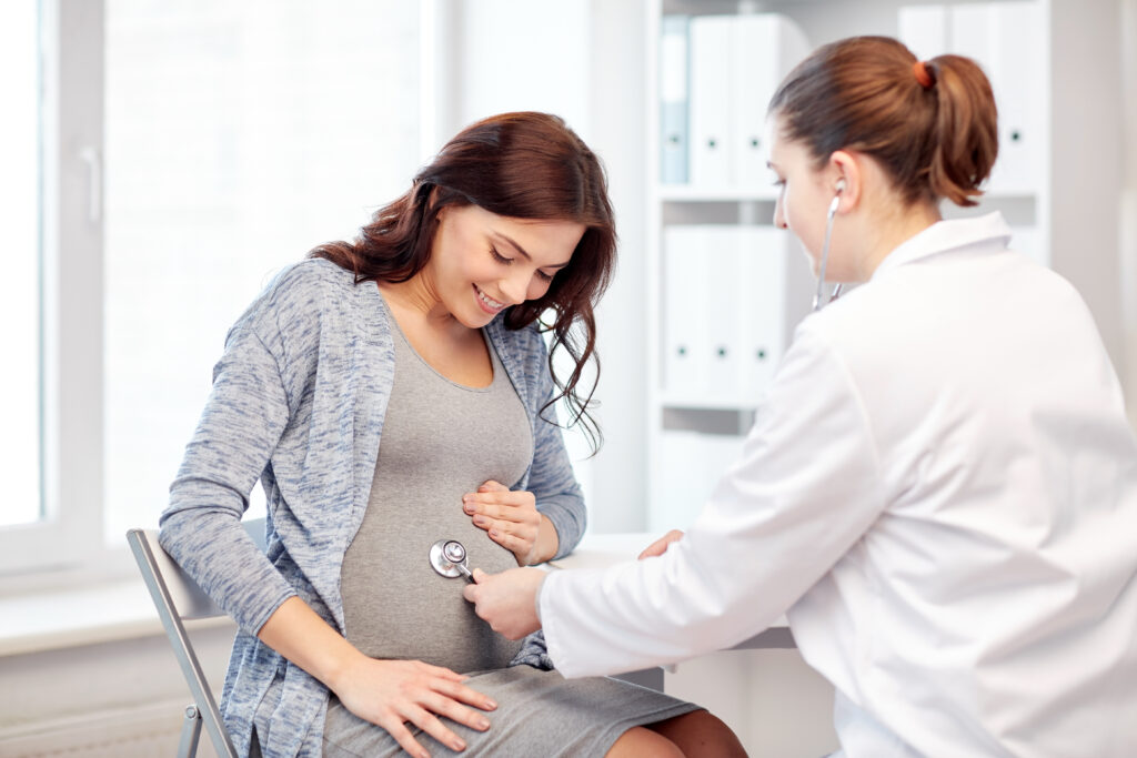a pregnant woman getting her health checked by a doctor who's using a stethoscope to check the baby's heartbeat