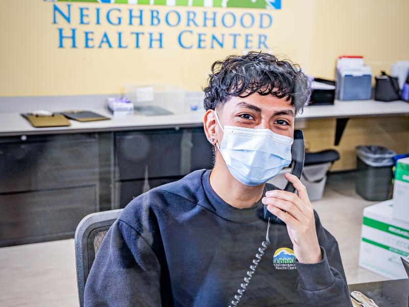 front desk receptionist wearing a mask while talking on the phone