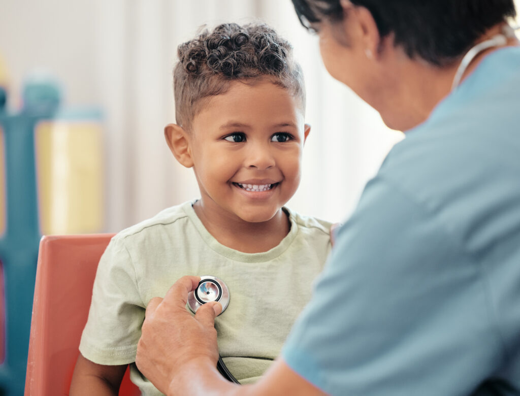a child smiling at the healthcare provider while they're checking their heart during a well child exam