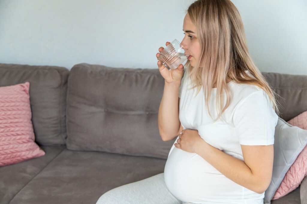 a pregnant woman sitting on a couch drinking a glass of water to see if she's experiencing true vs false labor