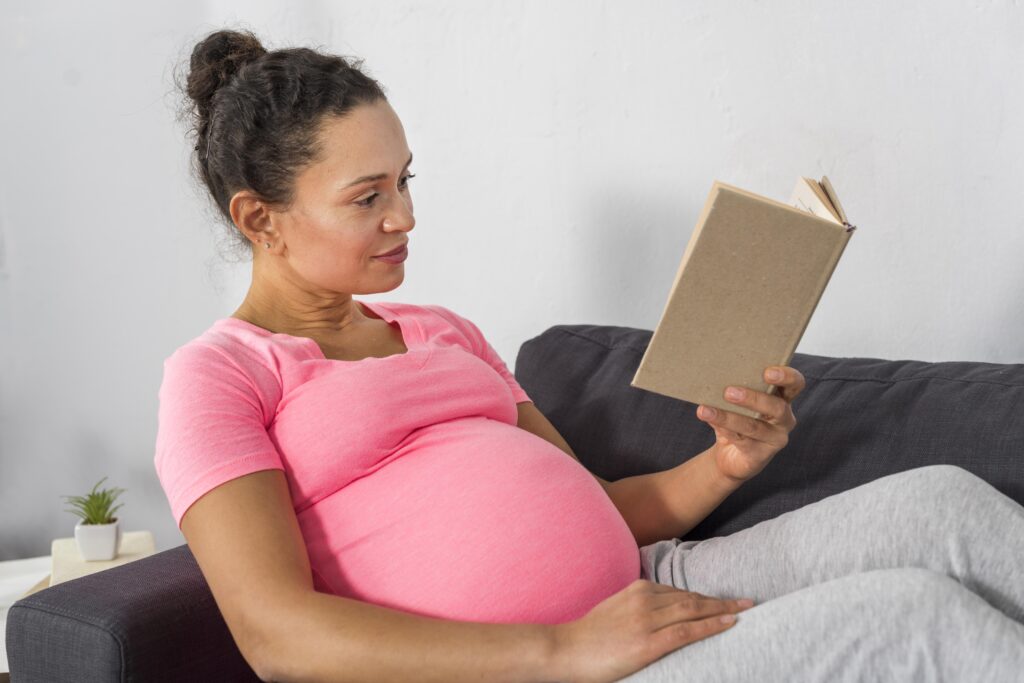 pregnant woman sitting on a couch reading a book