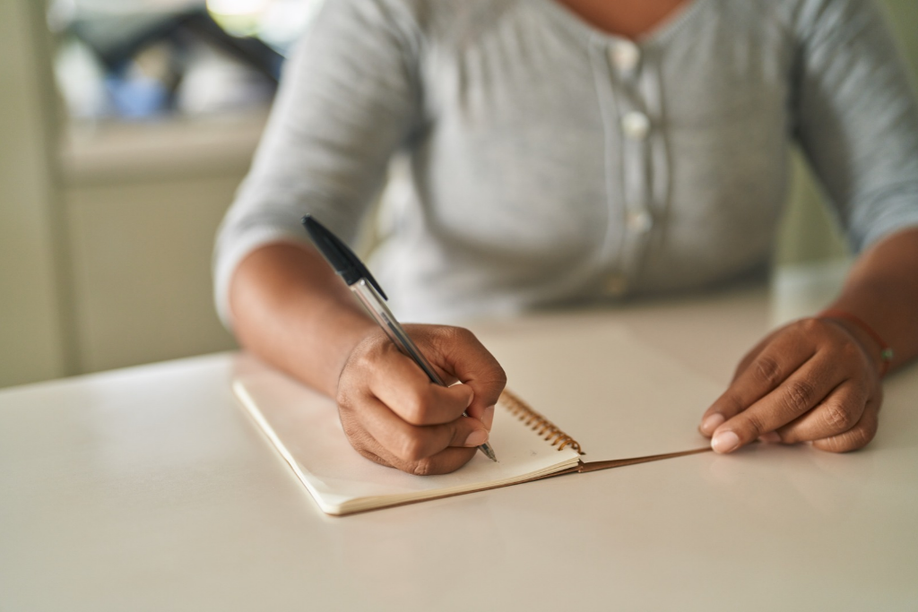 woman sitting at a table writing down her medical concerns in a notebook before her appointment